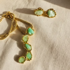 Gold necklace and earrings with green gemstones emeralds on a natural fabric background