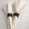 Two folded white napkins with Handwoven Iraca palm napkin rings.  Intricate lattice weave design, styled on soft neutral linen napkins, showcasing natural fibres and Artisan craftsmanship in elegant table décor.