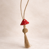 Handwoven mushroom charm. Decorative tassel with a red top and beige body on a light beige background
