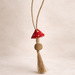 Handwoven mushroom charm. Decorative tassel with a red top and beige body on a light beige background