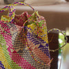 A colorful handwoven bucket bag with a drawstring closure and shoulder strap