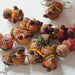 A group of small handwoven capybaras, decorated with colorful beanies and scarves in pink, green, orange, purple, and yellow.